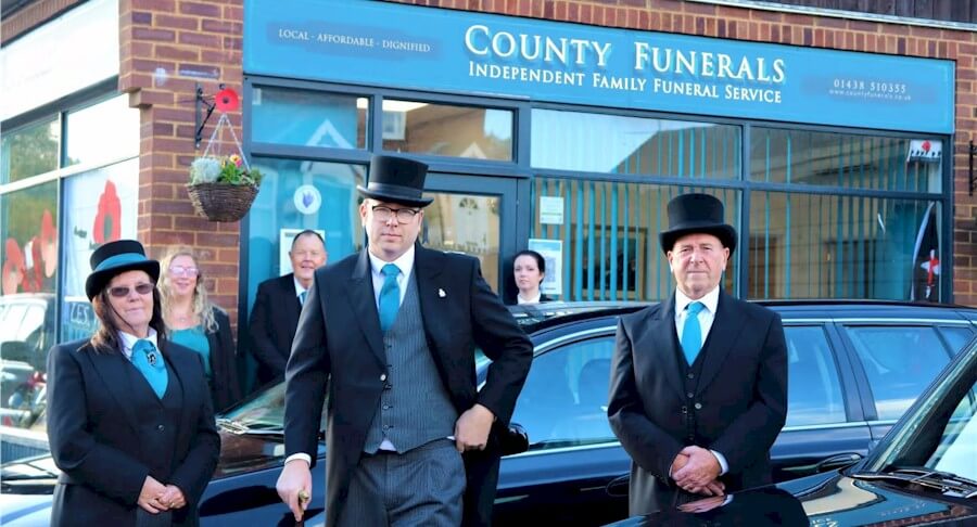 County Funerals team dressed professionally posing outside the office with vehicles.